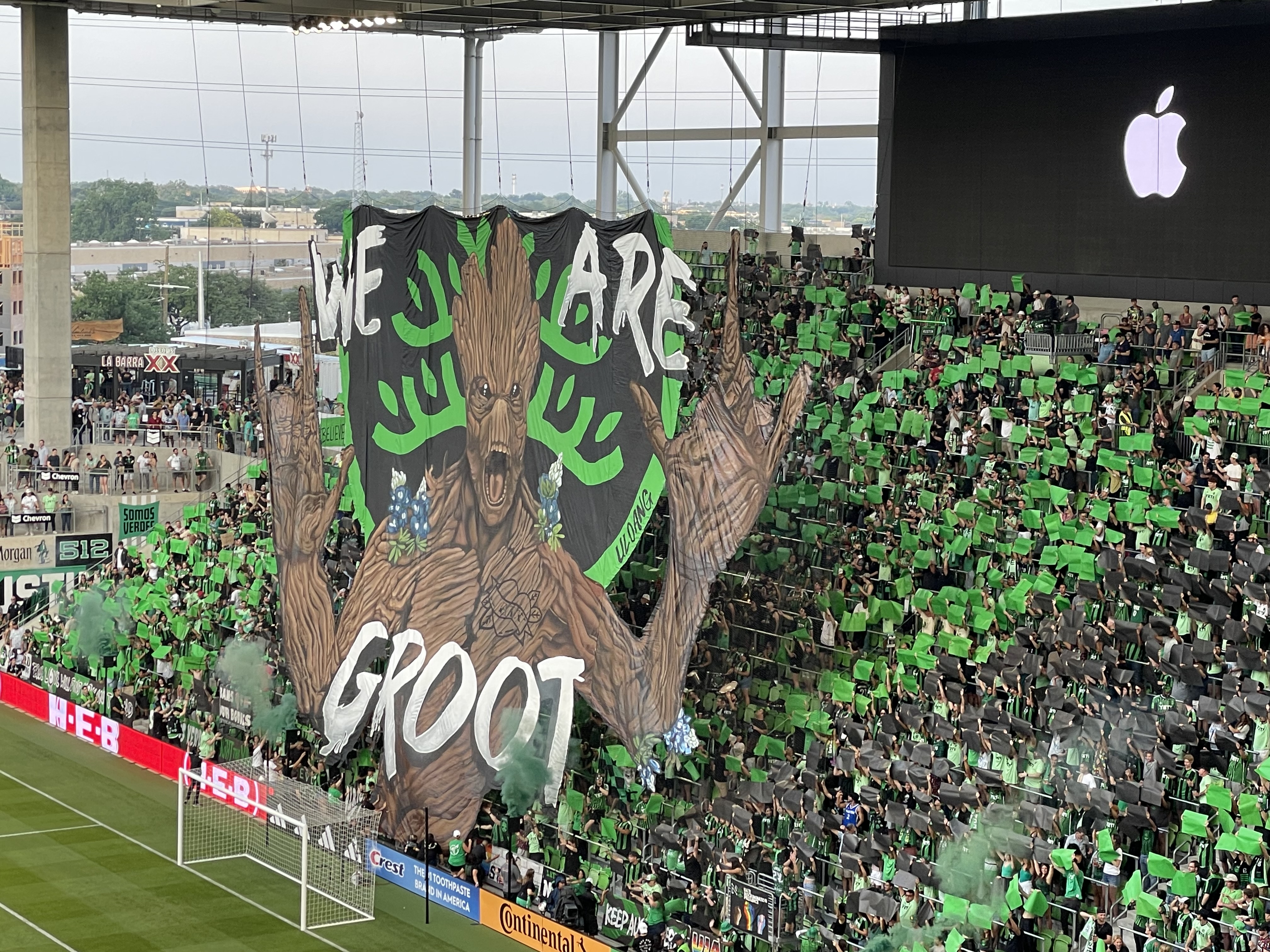 Austin Anthem supporters at Q2 Stadium unveiling a large tifo of a tree-like figure with the words "We are Groot," surrounded by fans holding up green cards in the stands.